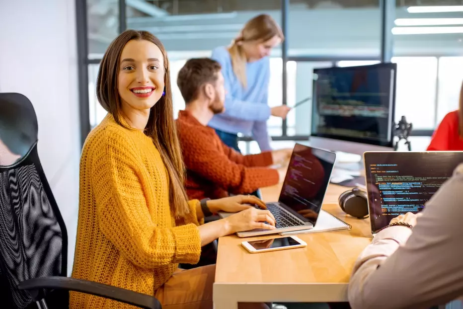 Femme souriante travaillant sur un ordinateur portable avec ses collègues travaillant autour d'elle